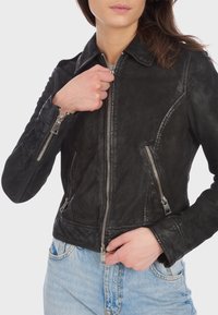 Giubbotto in pelle nera con colletto, dettagli con zip argentati e silhouette aderente. Presenta tasche con zip e finitura testurizzata.