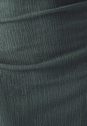Tekstūrēts zaļš audums ar ribotu rakstu, kurā redzami vertikāli līnijas, kas rada viļņveidīgu efektu. Mīksts, plūstošs materiāls.