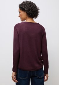 Paars lange mouwen sweater met een textuurafwerking, ronde halslijn en ribgebreide zoom, gecombineerd met donkerblauwe jeans met achterzakken.
