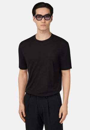 T-shirt nera a maniche corte realizzata in tessuto morbido, con un classico collo rotondo. Il modello l'ha abbinata a pantaloni scuri su misura e occhiali da sole.