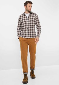 Kariertes Hemd in Braun, Creme und Marineblau; zwei Brusttaschen; kombiniert mit hellbraunen gerade geschnittenen Hosen; braune Schnürstiefel mit strukturierten Sohlen.