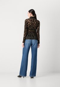 Een lange mouw leopardprint top van doorschijnende stof, gecombineerd met wijde blauwe jeans en zwarte haklaarzen.