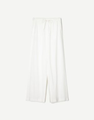 Witte wijde broek met een trekkoord in de taille, weergegeven tegen een effen achtergrond, wat de ontspannen stijl en de textuur van de stof benadrukt.