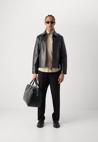 Sort læderjakke over en beige button-up skjorte, parret med sorte bukser og en struktureret sort taske. Glat tekstur, moderne design.