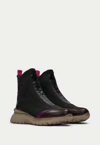 Botas de tobillo verdes y marrones con una cremallera negra brillante, acentos morados y una suela texturizada. Presenta un logo redondo en el lado.