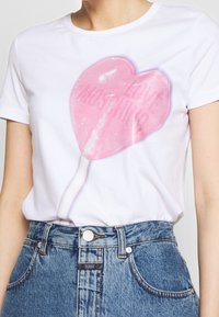 Bílý tričko s grafikou růžové srdcovité lízátko s textem "LOVE MOSCHINO." Krátké rukávy, jemný bavlněný materiál.
