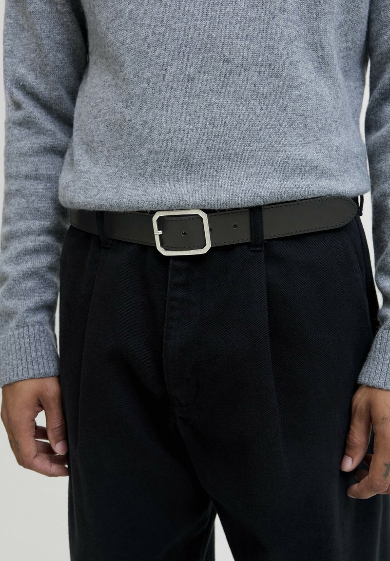 Black leather belt with a rectangular silver buckle, worn over black pants and under a grey knit sweater.