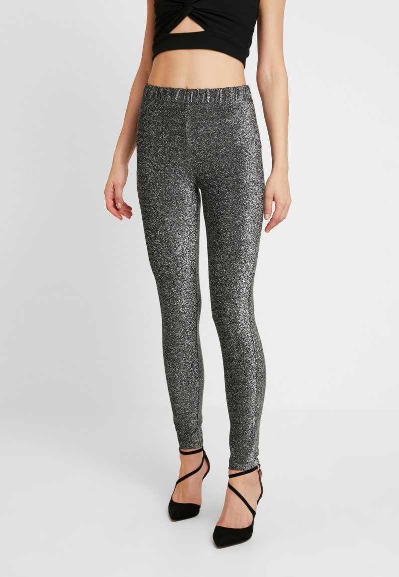 Leggings noirs à paillettes, taille haute, avec une ceinture élastique ; associés à des talons aiguilles noirs à lanières et un crop top ajusté.