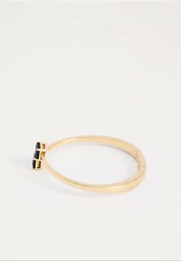 Zlata zapestnica z zapestnico z rektangelskim črnim kamnom na minimalističnem belem ozadju.