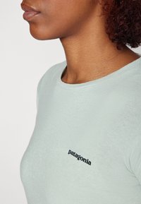 T-shirt ajusté bleu clair en tissu doux, avec un col rond et un logo noir "Patagonia" sur le côté gauche.