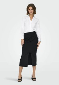 Witte blouse met lange mouwen, gecombineerd met een zwarte pinstriped rok tot de knie met een voorkniplijn, gedragen met zwarte hakken sandalen.