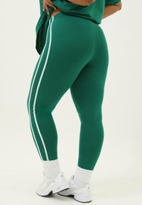 Gröna leggings med vita sidor, tillverkade av stretchigt material. De har en tight passform och är kombinerade med vita sportskor och ribbade strumpor.