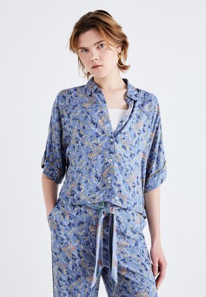 Chemise bleue à manches courtes en tissu léger avec un motif floral paisley, dotée d'une fermeture à boutons sur le devant et de manches retroussées.