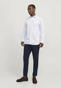 White long-sleeve shirt with a classic collar, paired with navy slim-fit trousers and brown suede shoes. Simple and clean design.