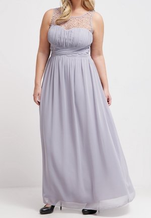 Woman wearing a floor-length lavender gown with sheer beaded neckline and pleated bodice, paired with black closed-toe heels.