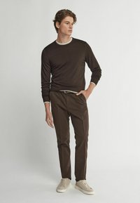 Brun långärmad tröja med en kontrasterande ljus halsringning, parat med mörkbruna byxor och beige sneakers. Enkelt mönster, figurnära stil.