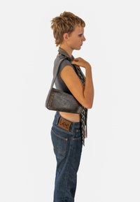 Borse in pelle grigia a forma triangolare, con il nome del marchio "EXPATRIÉ" in rilievo e in oro, abbinata a una sciarpa a motivi bianco e nero e jeans blu.