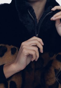 Bunda z umělé kožešiny s černým límcem na zip, hnědým tělem s leopardím potiskem a strukturovaným látkovým detailem.