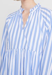 Gestreiftes Kleid in Blau und Weiß mit einem Rüschkragen, V-Ausschnitt und gerafftem Rock. Hergestellt aus leichtem Stoff und mit einer lässigen Passform.
