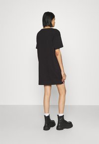Svart oversized t-skjortekjole med korte ermer, rund hals og en liten detalj nær kanten. Brukt med kraftige svarte snørestøvler.