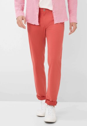 Heren tapered-fit broek in koraalstof, met een gladde textuur, voorzakken en opgerolde boorden, gecombineerd met witte sneakers.