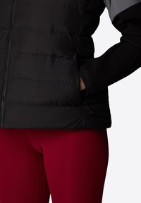 Svart isolert jakke med grå skulderpanel og glidelås. Har fleece mansjetter og justerbar hem. Kombinert med røde leggings.