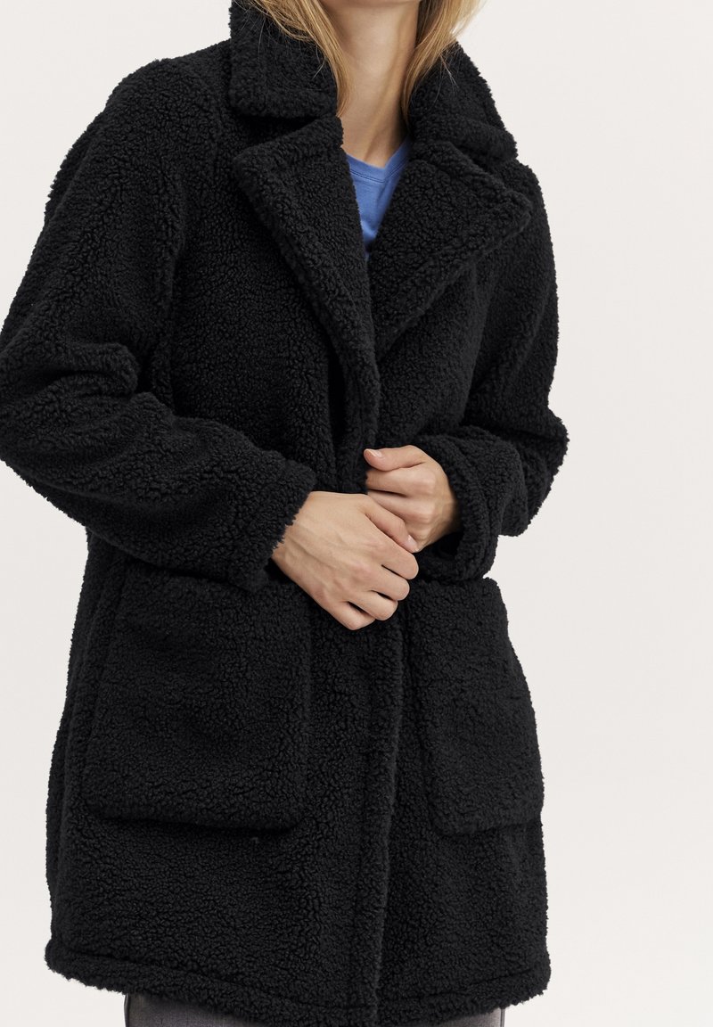 Black fleece coat with a textured, soft surface, featuring a notched collar, two front pockets, and a relaxed fit.