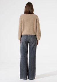 Beige, fuzzy trui in combinatie met hoogtijdelijke, wijde donkergrijze jeans. Opvallende stiksels op de jeans en een relaxte pasvorm van de trui.
