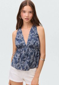 Námořnický top bez rukávů s květinovým vzorem a hlubokým výstřihem do V, se staženým pasem. Lehký materiál; zkombinovaný s bílými šortkami s třásněmi.
