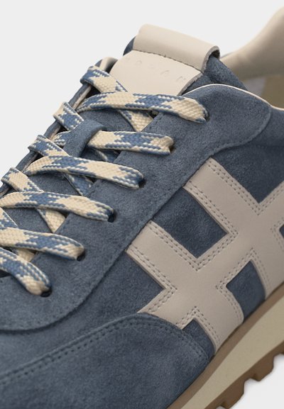 Μπλε σουέτ αθλητικό παπούτσι με σχέδιο σταυρού σε κρεμ απόχρωση, κορδόνια υφαντά σε κρεμ-μπλε και μπεζ σόλα, εμφανίζοντας το πάνω μέρος και τις λεπτομέρειες των κορδονιών.
