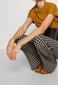 T-shirt manches courtes moutarde associée à un pantalon large à carreaux noir et beige. Des sandales roses scintillantes à semelle épaisse complètent la tenue.