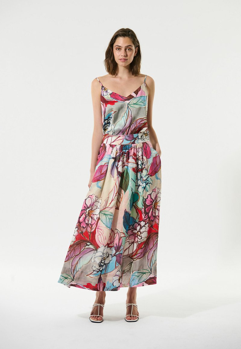Robe maxi en coton à fleurs avec un décolleté en V, des bretelles ajustables et une taille élastique. Présente des feuilles et des fleurs colorées sur un fond clair.