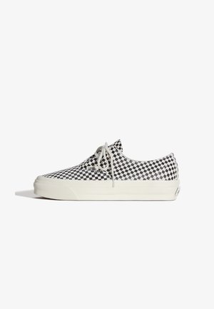 Baskets basses avec un motif à damier noir et blanc, lacets blancs et semelle en caoutchouc blanche épaisse, vues de profil sur fond blanc.