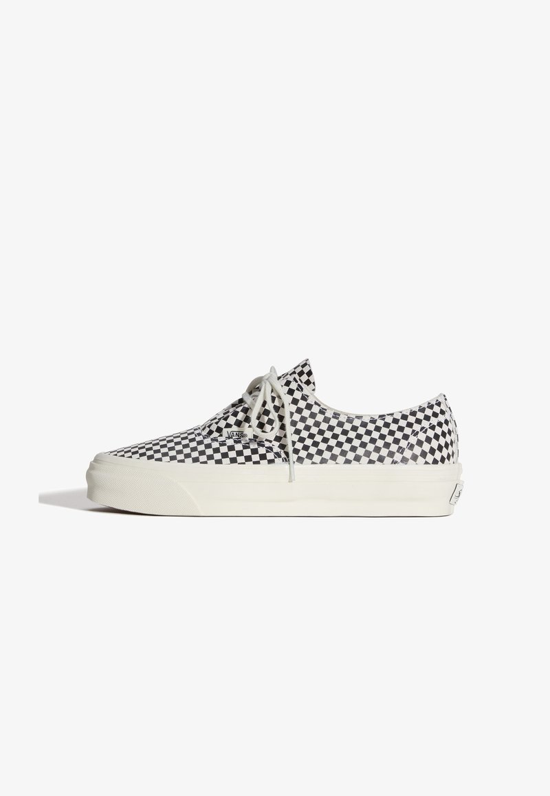 Baskets basses avec un motif à damier noir et blanc, lacets blancs et semelle en caoutchouc blanche épaisse, vues de profil sur fond blanc.