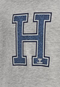 Sudadera gris con un gran logotipo en relieve de color azul "H" con un contorno azul oscuro, y un pequeño logotipo de "hummel" en la esquina inferior.