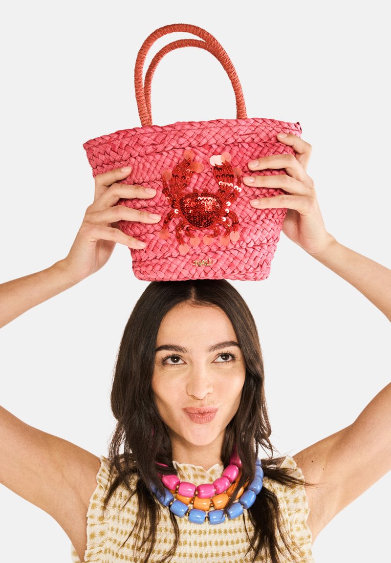 Rosa vävd korgväska med två handtag, med en paljetterad krabba-design. Väskan har en texturerad yta och en guldlogotypdetalj i botten.