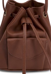 Sac à cordon en cuir marron avec une texture lisse. Comprend une poche avant et des œillets métalliques. Conception du dessus fortement resserrée.