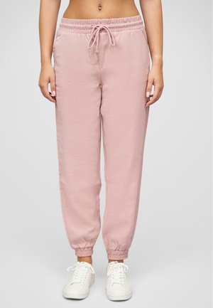 Pantalons de survêtement rose clair, taille élastique avec cordon de serrage réglable, poignets côtelés et coupe loose, associés à des baskets blanches.