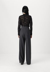 Black lace long-sleeve top paired with high-waisted, wide-leg dark gray trousers and square-heeled shoes, viewed from the back.
