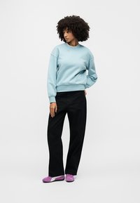 Ανοιχτό μπλε φούτερ, μαύρο παντελόνι με φαρδιά μπατζάκια και μοβ αθλητικά παπούτσια. Το φούτερ έχει στρογγυλή λαιμόκοψη· το παντελόνι έχει άνετη εφαρμογή.