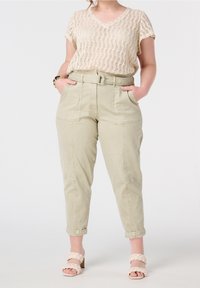 Haut en crochet beige à manches courtes, associé à un pantalon léger vert ceinturé avec des poches latérales. Sandales à talons tressées rose clair.