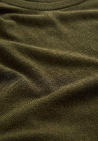 Olivově zelený svetr má měkkou texturu, pružný výstřih a hladký, mírně lesklý povrch. Látka vypadá čistě a kvalitně zpracovaná.