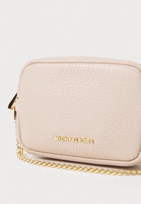 Beige leather crossbody bag with a textured surface, featuring a gold chain strap and embossed "MICHAEL KORS" logo on the front.