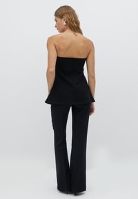 Černý bezramínkový peplum top s přiléhavým tělem; spárovaný s černými rozšířenými kalhotami. Hladká textura, minimalistický design a žádný viditelný kovový hardware.