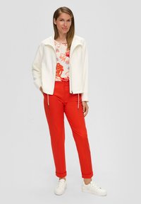 Witte ritsjack met hoge kraag, bloemenpatroon top, helderrode broek en witte sneakers. Glad textuur en casual ontwerp.