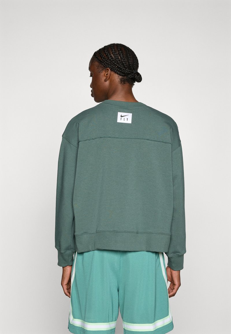 Felpa verde scuro con vestibilità comoda, polsini a coste e un'etichetta bianca con "Nike FLY" sulla parte superiore della schiena. Abbinata a pantaloni corti verde menta.