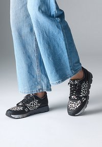 Baskets noires de sport avec un motif léopard, dotées d'une superposition texturée et de semelles plates, associées à un pantalon en denim bleu ample.