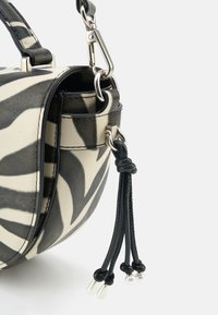 Runde Handtasche mit einem schwarz-weißen Zebra-Muster, strukturiertem, fellähnlichem Material, silbernen Beschlägen und einer dekorativen schwarzen Quaste mit Perlen.