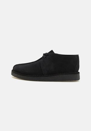 Chaussure en daim noir avec un design à bout rond, un devant à lacets et une semelle en caoutchouc texturée. Présente des coutures minimales et une finition lisse.