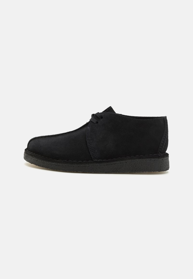 Chaussure en daim noir avec un design à bout rond, un devant à lacets et une semelle en caoutchouc texturée. Présente des coutures minimales et une finition lisse.